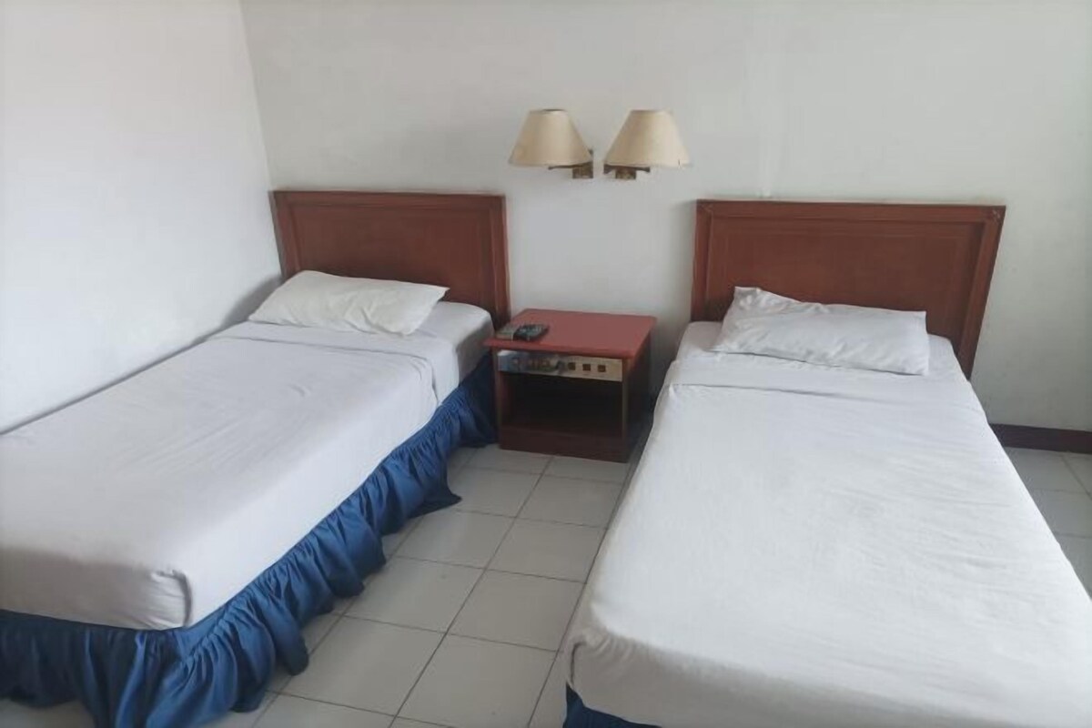 Una habitación de hotel con dos camas individuales, una mesita de noche con lámpara y una pequeña mesa.