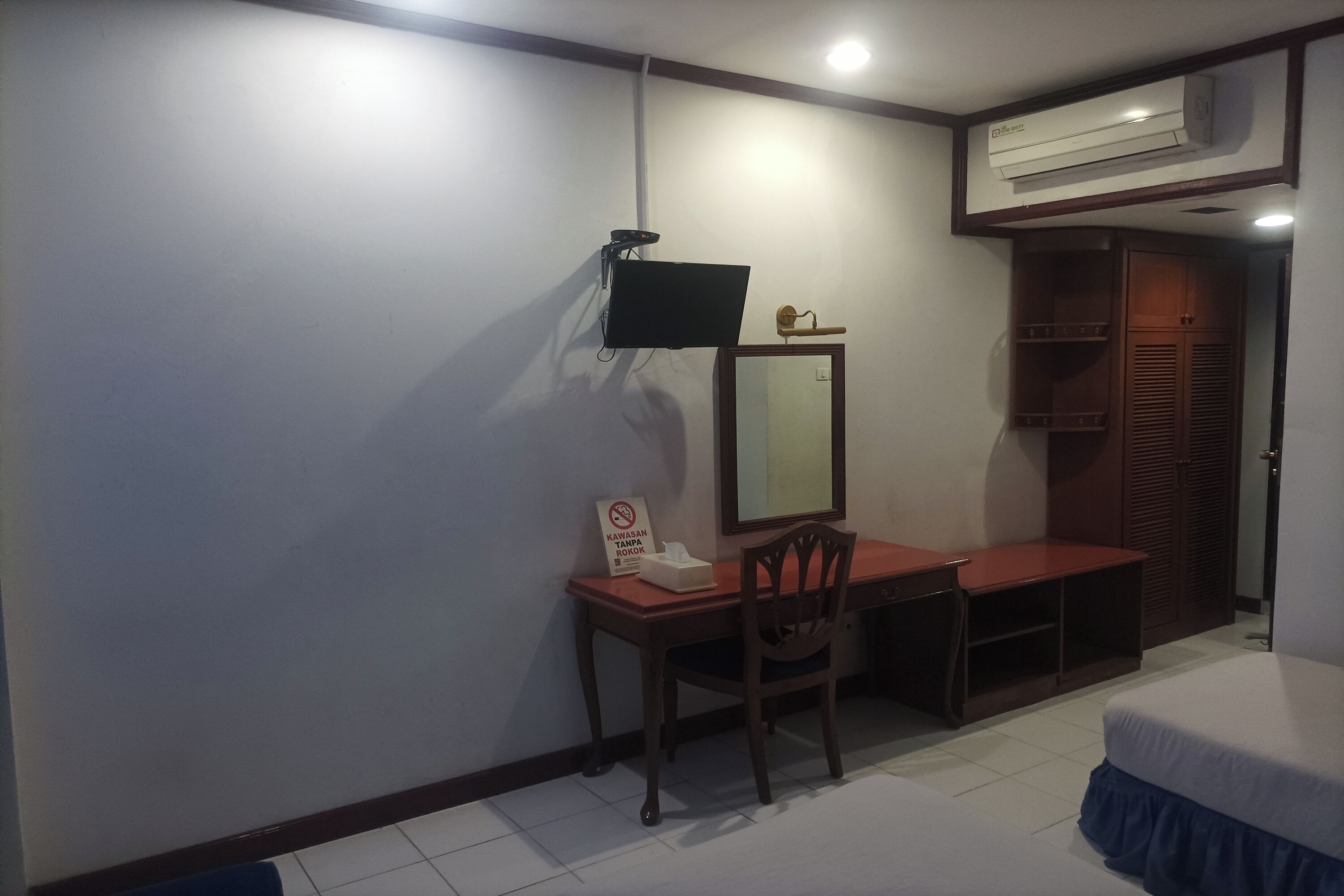 Un dormitorio con cama, escritorio, silla, televisor montado en la pared y armario.