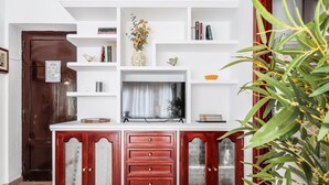 A wooden cabinet with glass doors, a white shelf unit above it, and a plant to the right. - Pure Seville elegance and comfort (Sevilla)