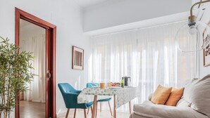 A living room with a sofa, a dining table with chairs, a potted plant, and a window with sheer curtains. - Pure Seville elegance and comfort (Sevilla)