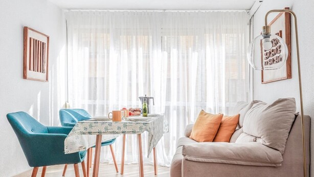 A bright living room with a sofa and chairs, a dining table with a coffee machine, and a large window with sheer curtains. - Pure Seville elegance and comfort (Sevilla)