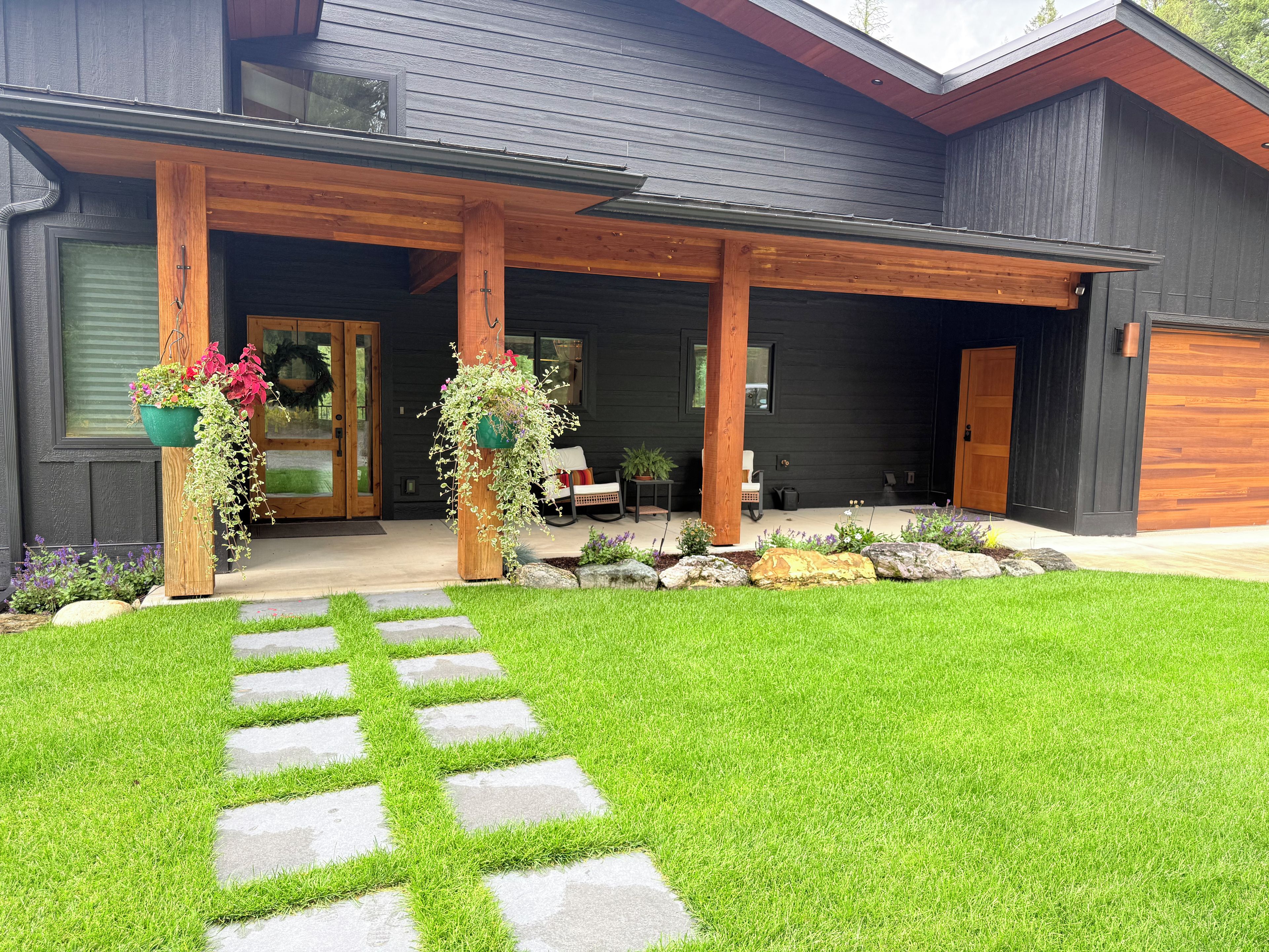 A modern house with a covered porch, stone pathway, and potted plants.