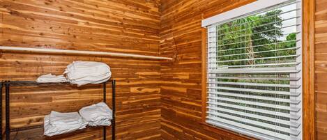 Ein Eckzimmer mit Holzwänden, einem Fenster mit Rollläden und einem Metallgestell mit gefalteten Handtüchern.