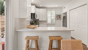 Una cocina moderna con armarios blancos, una isla grande con taburetes y vistas al exterior.