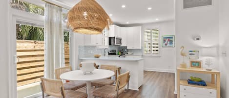 A modern kitchen with white cabinets, a central island, and a dining area with wicker chairs.