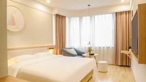 Una habitación de hotel con una cama grande, un escritorio, una silla, una mesita y un televisor montado en la pared.
