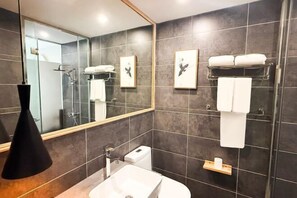Ein modernes Badezimmer mit großem Spiegel, weißem Waschbecken, einer Duschkabine aus Glas und einem Handtuchhalter.