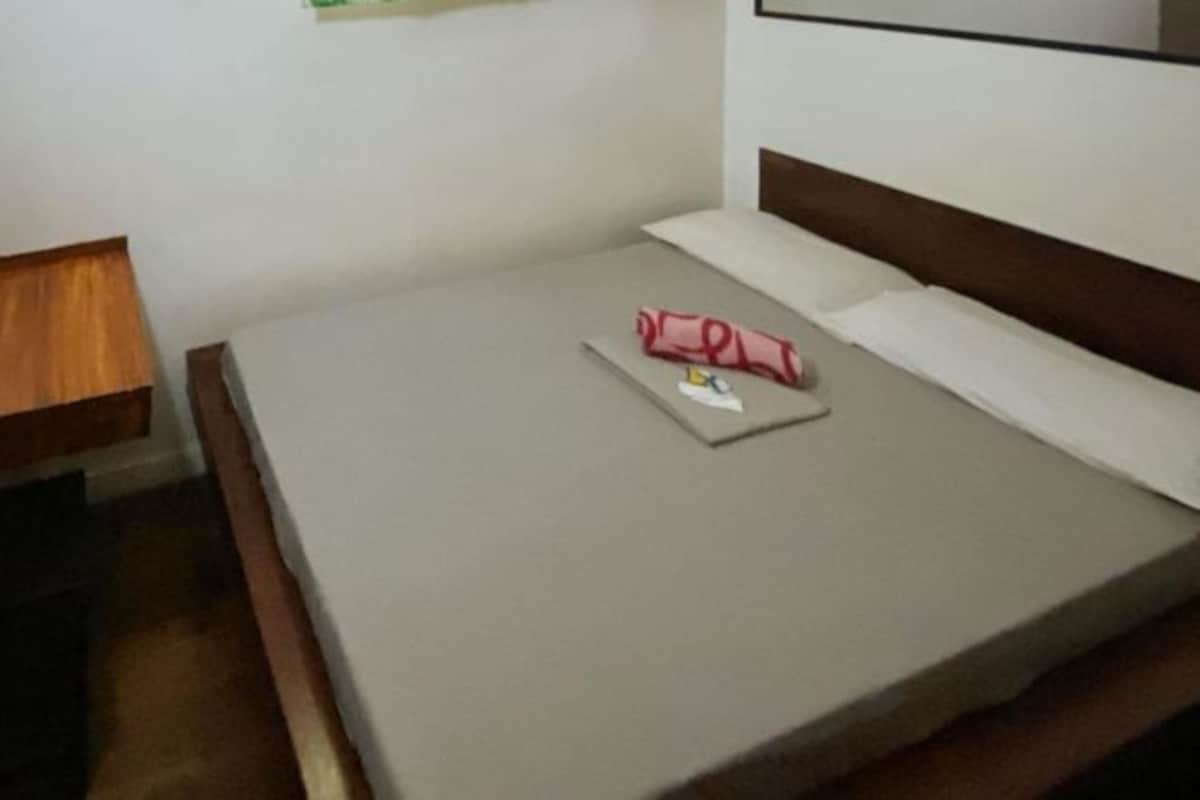 A small, neatly made bed with a wooden headboard, a single pillow, and a rolled-up towel on the bed.