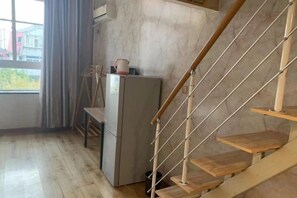 A room with a wooden staircase, a refrigerator, and a window with curtains. - Xiaisi Lexiang Service Apartment (Dalian Xinghai Square) (Dalian)