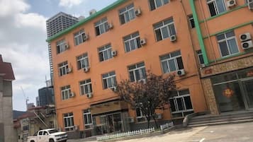 A multi-story building with a flat facade, multiple windows, and a parking area with a white pick-up truck.