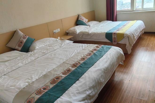 Quarto de hotel com duas camas, piso de madeira e janela com cortinas.
