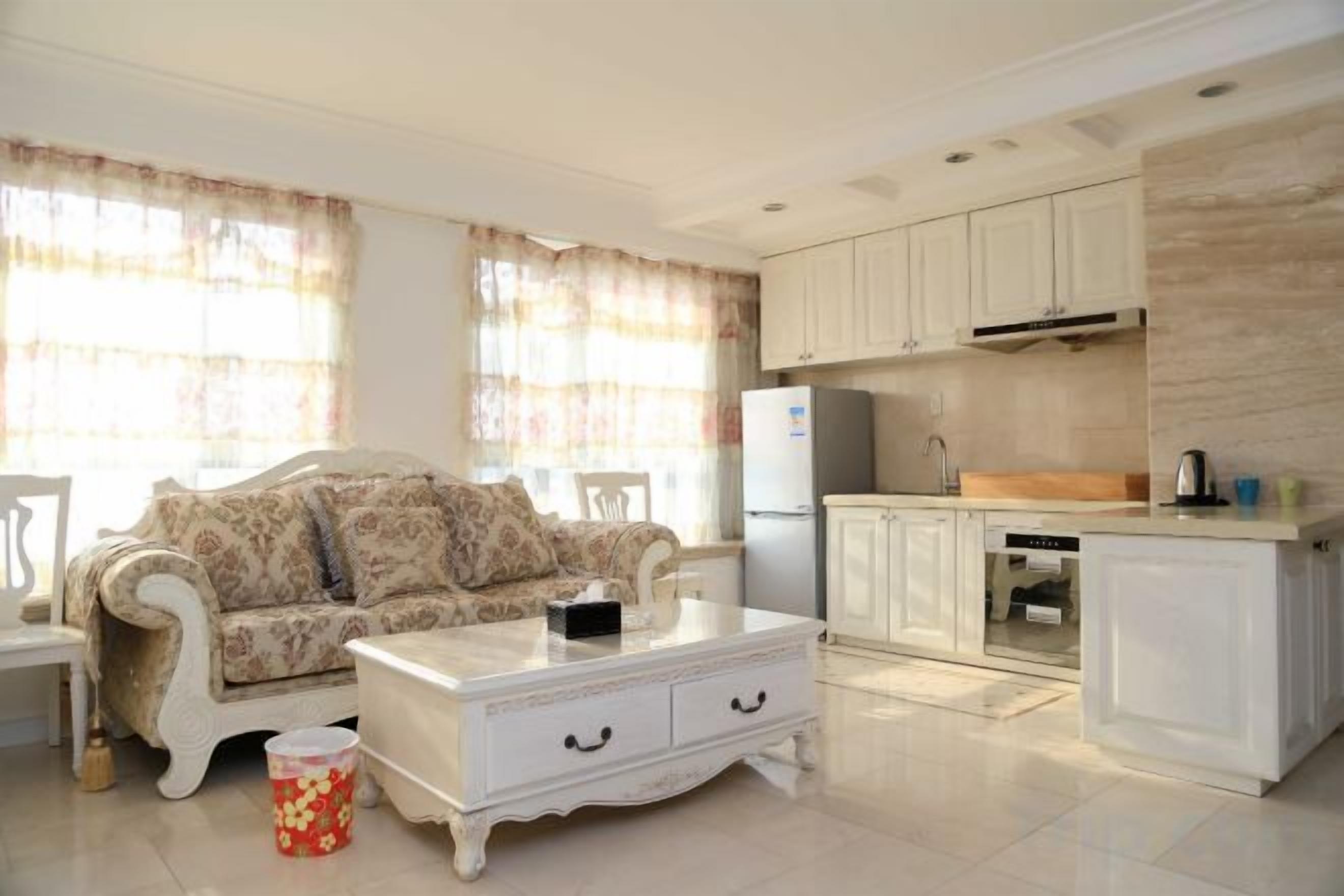 Una sala de estar con sofá, mesa de centro y una pequeña cocina con alacenas y refrigerador.