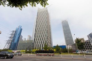 A modern high-rise building with a distinctive geometric facade, surrounded by other tall buildings and a street with vehicles. - Xiaisi Lexiang Service Apartment (Dalian Xinghai Square) (Dalian)