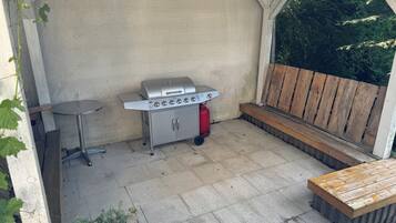 Une terrasse avec un barbecue, une petite table ronde et un banc en bois.