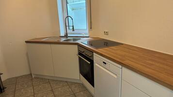 Une cuisine compacte équipée d’un évier, d’une cuisinière et d’un lave-vaisselle, avec un plan de travail en bois et un sol carrelé.