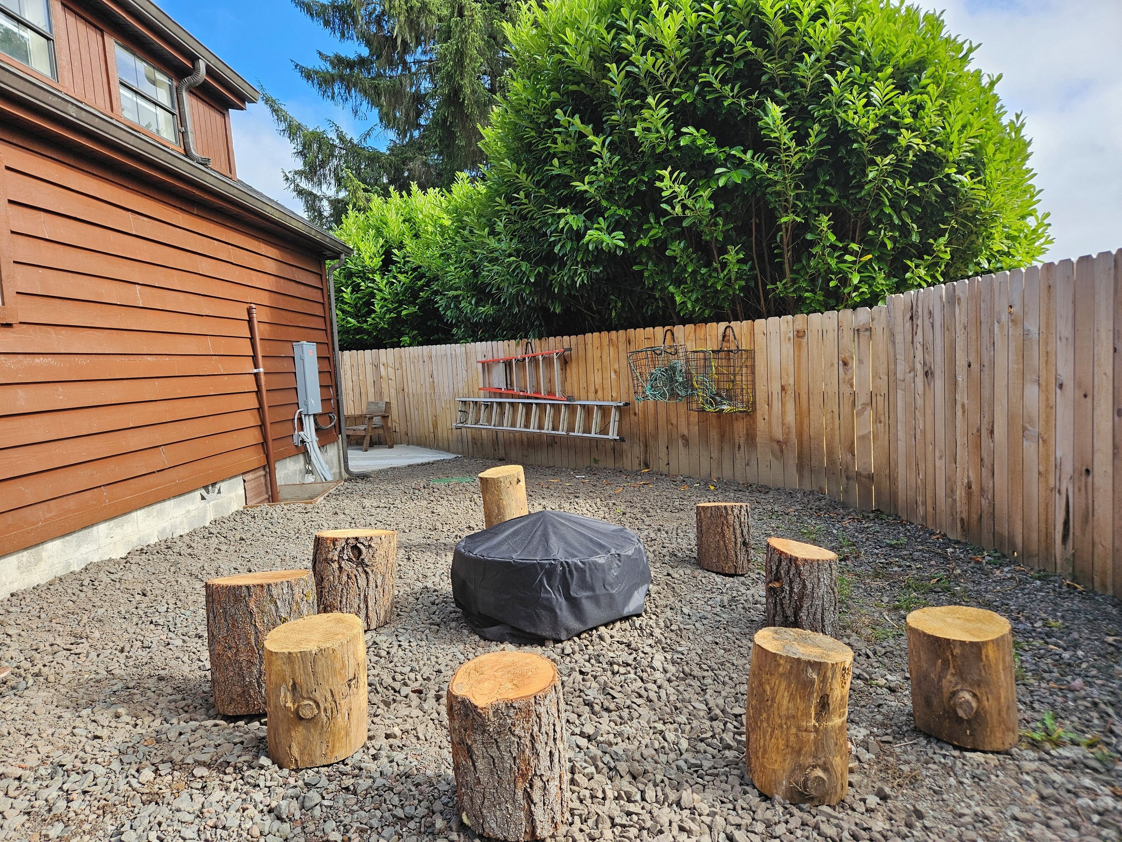 Un jardin avec une terrasse en bois, un coin salon extérieur avec des meubles noirs et une clôture en bois.