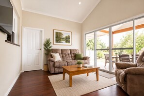 A living room with a brown sofa, a wooden coffee table, and a large sliding glass door leading to an outdoor area. - Driftwood Cottage (Busselton)