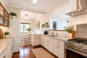 A modern kitchen with white cabinetry, a gas stove, a built-in oven, a dining area with a table and chairs, and a ceiling fan.