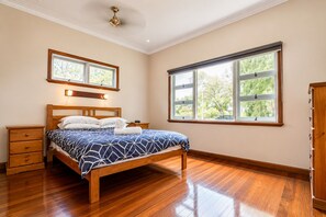 Ein Schlafzimmer mit einem hölzernen Bett, einem Nachttisch, einer Kommode und einem großen Fenster mit Blick auf Bäume.