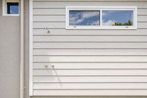 Un bâtiment avec un revêtement extérieur horizontal, une petite fenêtre donnant sur le ciel et un luminaire fixé au mur.