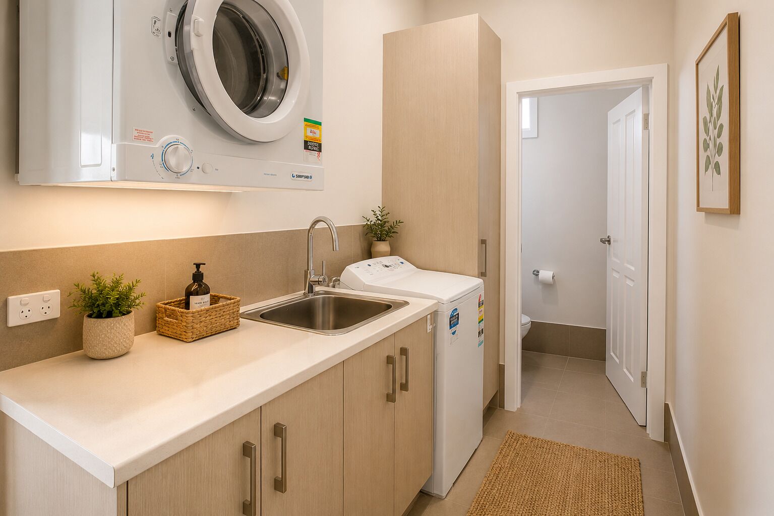 Une cuisine compacte équipée d’un lave-linge intégré, d’un évier et d’une petite plante en pot.