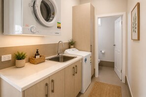 A compact kitchen with a built-in washing machine, a sink, and a small potted plant.