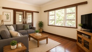 A living room with a sofa, coffee table, TV, and large windows. - Driftwood Cottage (Busselton)
