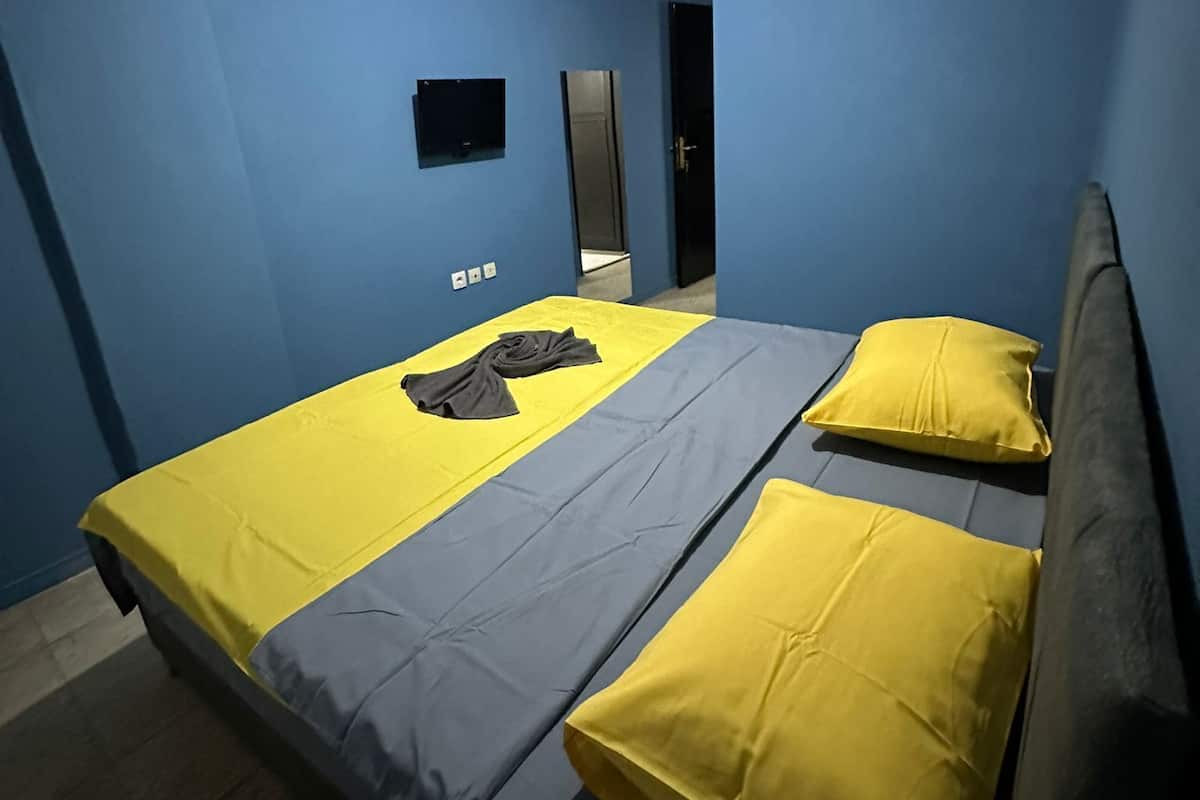 Ein Schlafzimmer mit einem Bett, zwei Kissen, einem Nachttisch, einem Spiegel und einem an der Wand befestigten Fernseher.