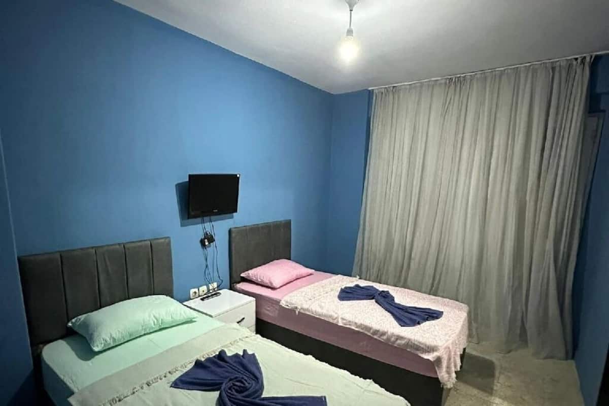 Ein Zimmer mit zwei Betten, einem Flachbildfernseher, einer Deckenleuchte und einem fenster mit Vorhängen.