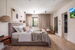 Een moderne slaapkamer met een groot bed, een nachtkastje, een tv aan de muur en een raam met gordijnen.