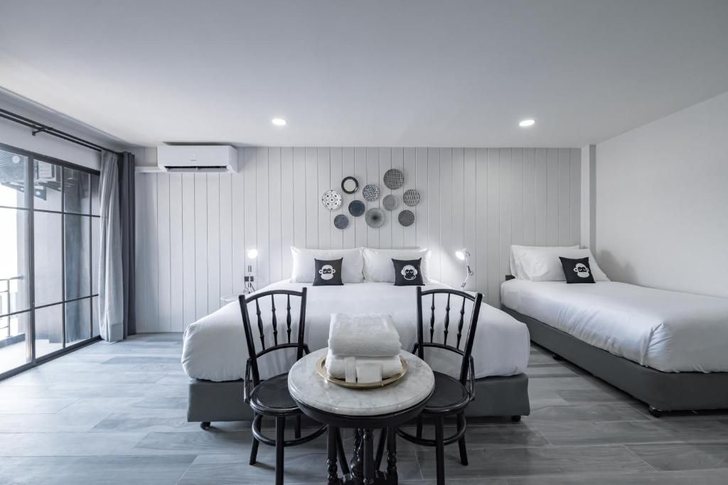 A modern hotel room with a large bed, a smaller bed, a dining table with chairs, and a large window.