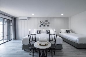 Ein modernes Hotelzimmer mit einem großen Bett, einem Einzelbett, einem Esstisch mit Stühlen und einem großen Fenster.