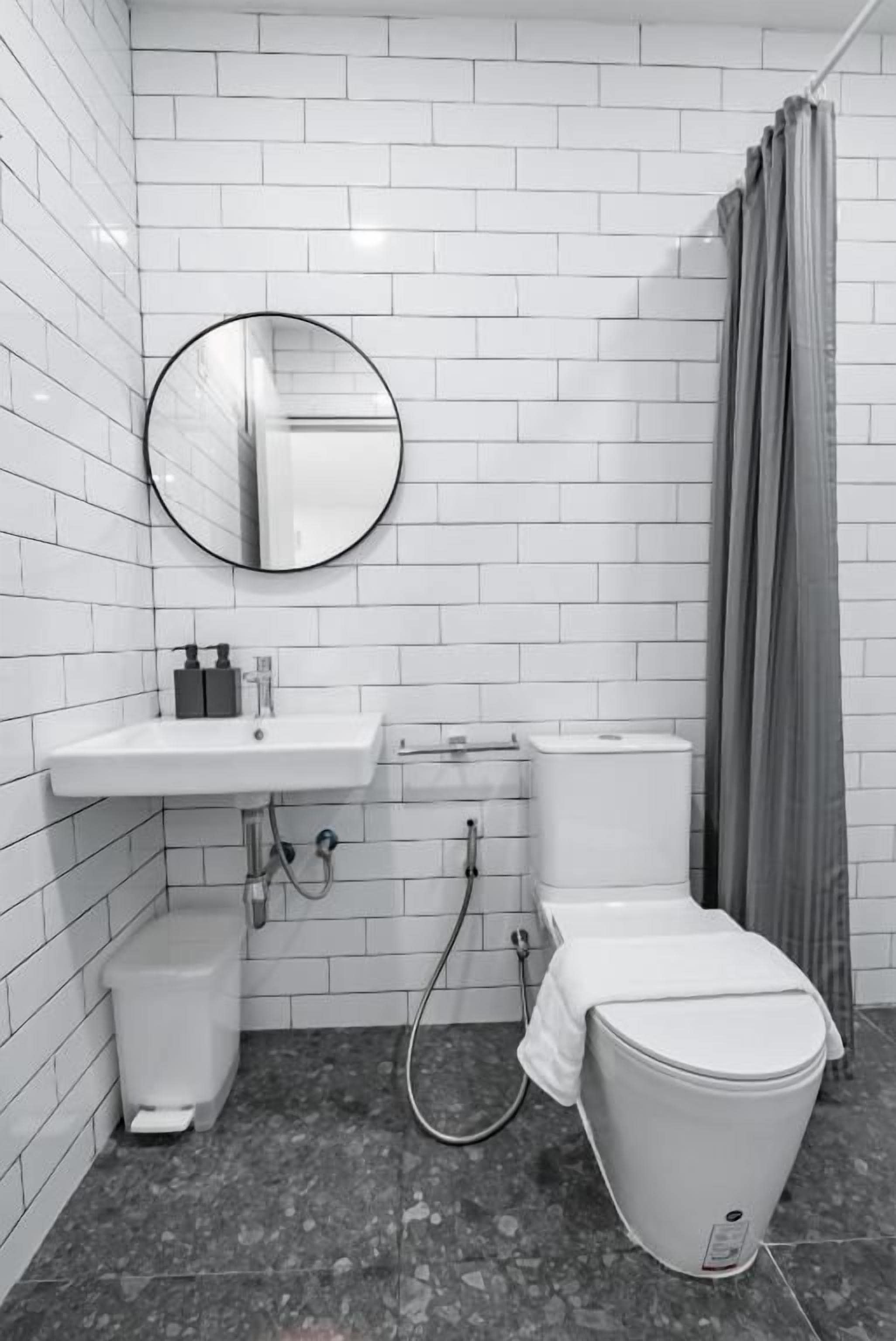 A bathroom with white tiled walls, a round mirror, a sink, a toilet, and a shower curtain.
