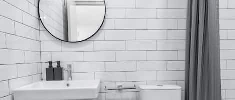 Un baño con paredes de azulejos blancos, un espejo redondo, un lavamanos, un inodoro y una cortina de ducha.