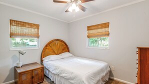 A bedroom with a bed, a nightstand, a wooden headboard, two windows with blinds, a ceiling fan, and a carpeted floor. - Mid-Century Gainesville Getaway: 3 Mi to UF Campus (Gainesville)