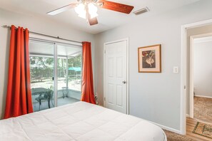 Un dormitorio con una cama grande, un ventilador de techo, una puerta corrediza de vidrio a un patio y un cuadro en la pared.