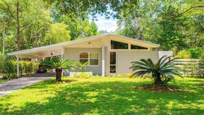A single-story house with a covered porch, surrounded by lush greenery and trees. - Mid-Century Gainesville Getaway: 3 Mi to UF Campus (Gainesville)