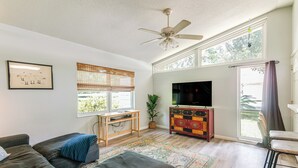A living room with a sofa, ottoman, TV, and a ceiling fan. - Mid-Century Gainesville Getaway: 3 Mi to UF Campus (Gainesville)