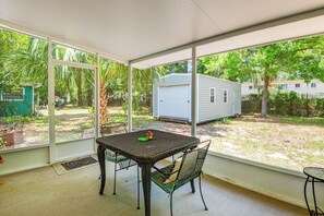 Un porche cubierto con una mesa y sillas, vista a una casa móvil y un patio cercado.