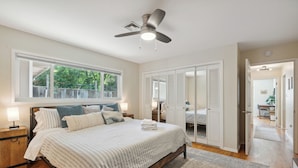 Ein Schlafzimmer mit Bett, Nachttischen, Deckenventilator, Fenster und Kleiderschrank.