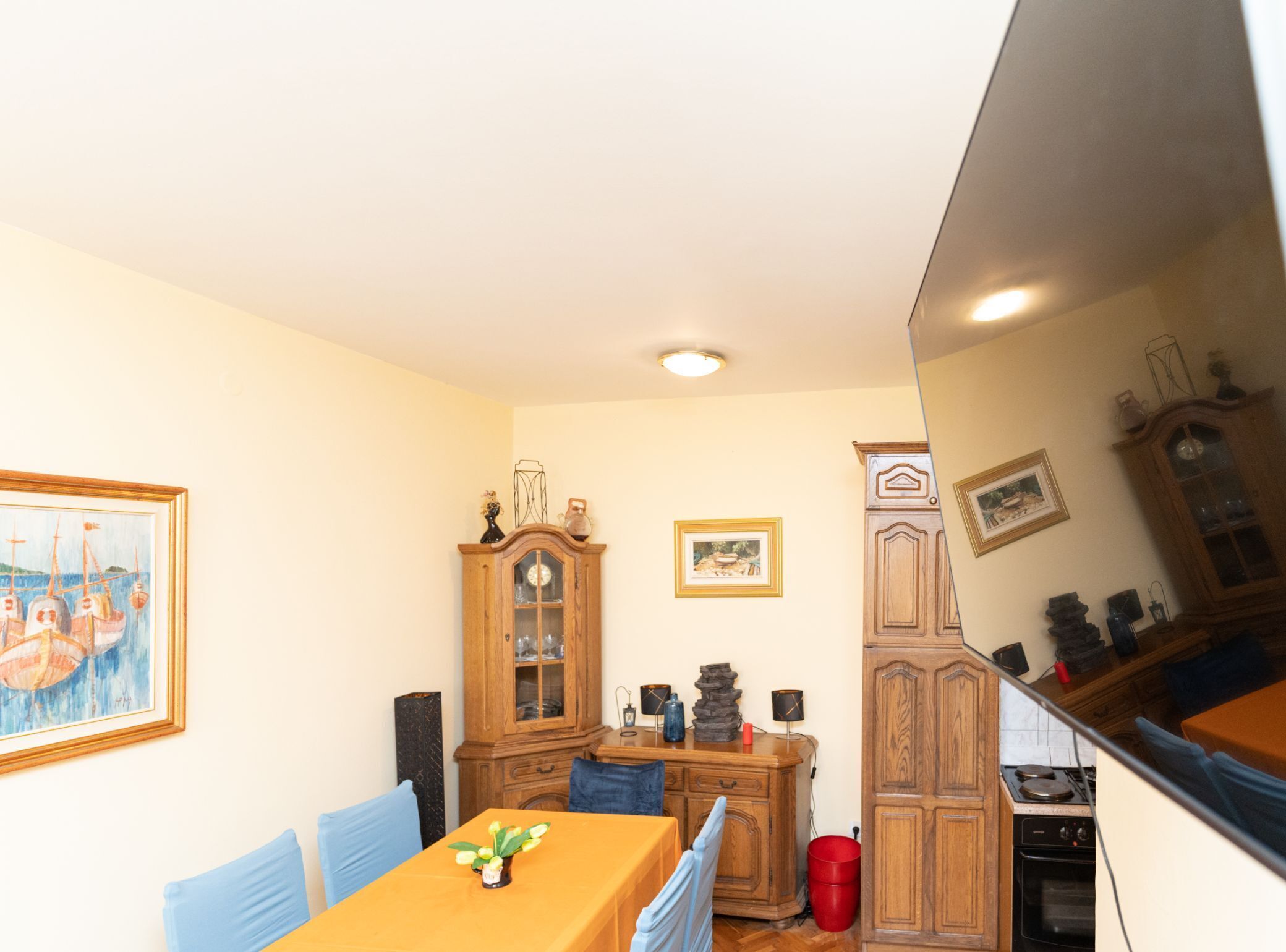A dining area with a wooden table, blue chairs, a cabinet with glass doors, and a painting on the wall.