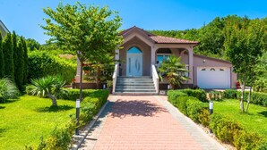 A two-story house with a red-tiled roof, a front entrance with a set of stairs, and a driveway leading to a garage. - Villa Mia 2 (Podbablje)