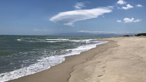 A beach with waves, a clear sky, and distant mountains.