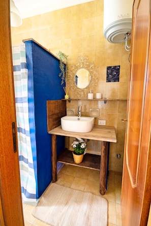 Ein Badezimmer mit einem Holzkosmetikschrank, einem weißen Waschbecken, einem Spiegel und einer Duschkabine.