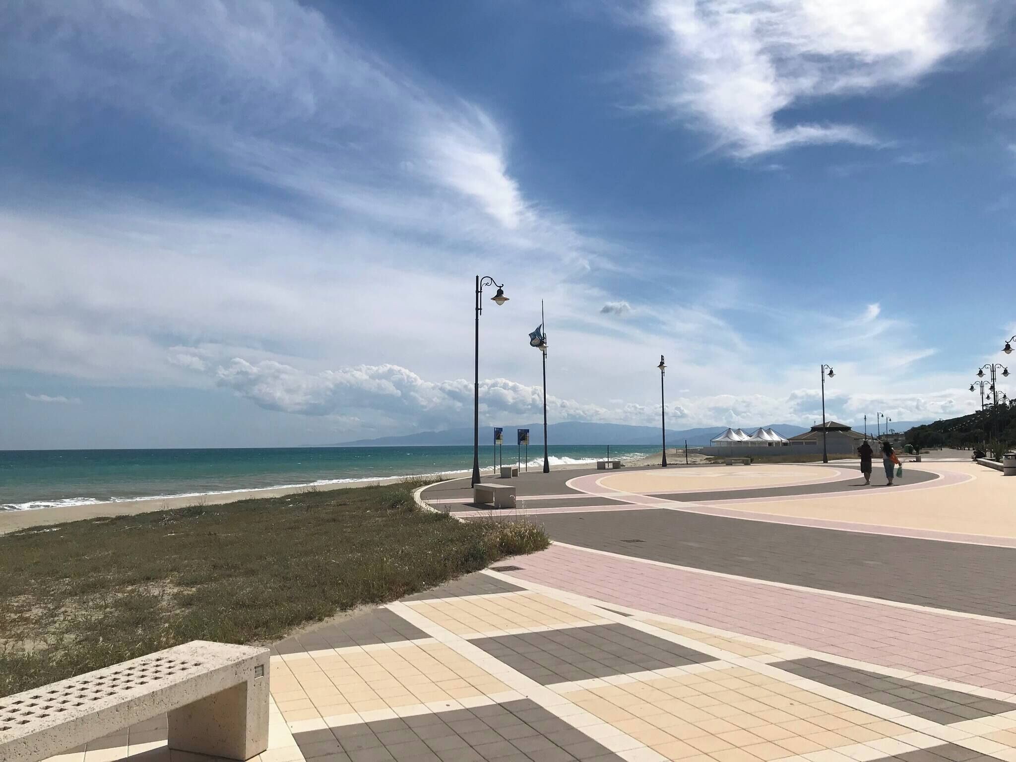 Eine Küstenpromenade mit gewundener Uferpromenade, Bänken, Straßenlaternen und Blick auf das Meer.