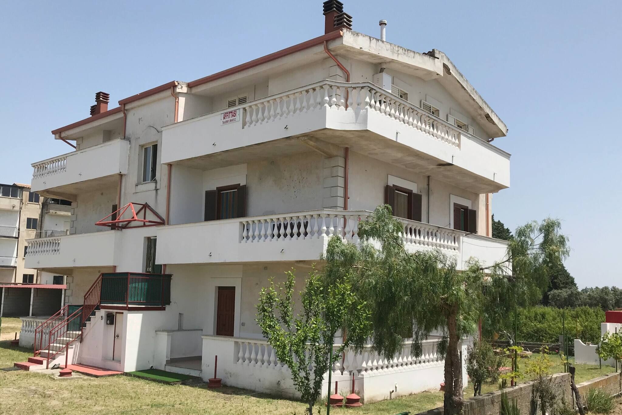 A multi-story building with balconies, a staircase, and a small garden area.