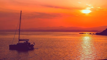Un coucher de soleil sur une mer calme, avec un voilier à l'horizon.
