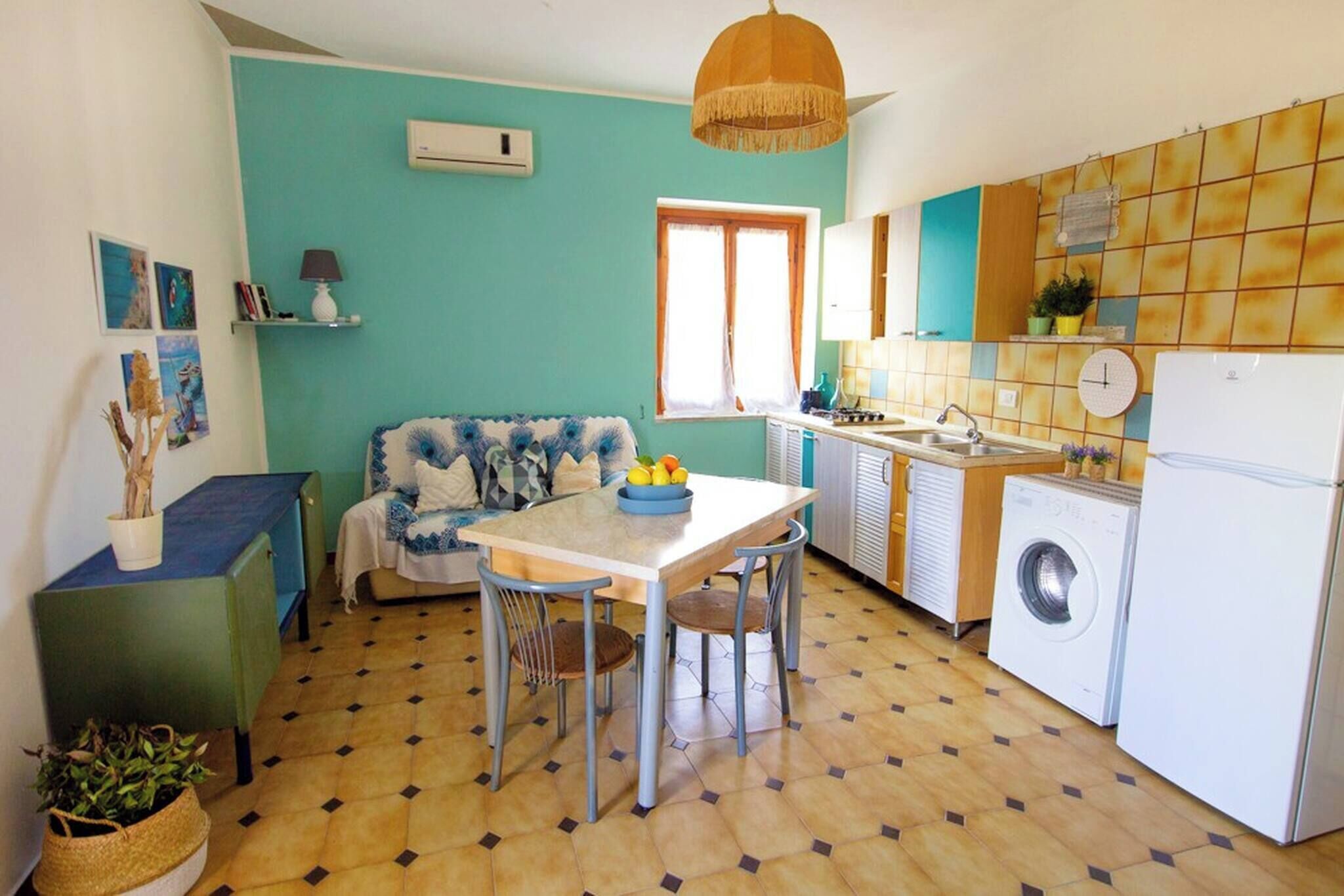 A compact kitchen with a dining table, chairs, a washing machine, and a sofa.
