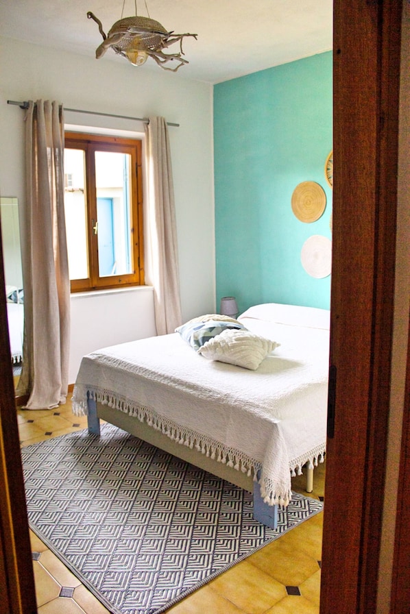 Ein Schlafzimmer mit Bett, einem Fenster mit Vorhängen, einem gemusterten Teppich und einer Wand mit einer runden Dekoration.