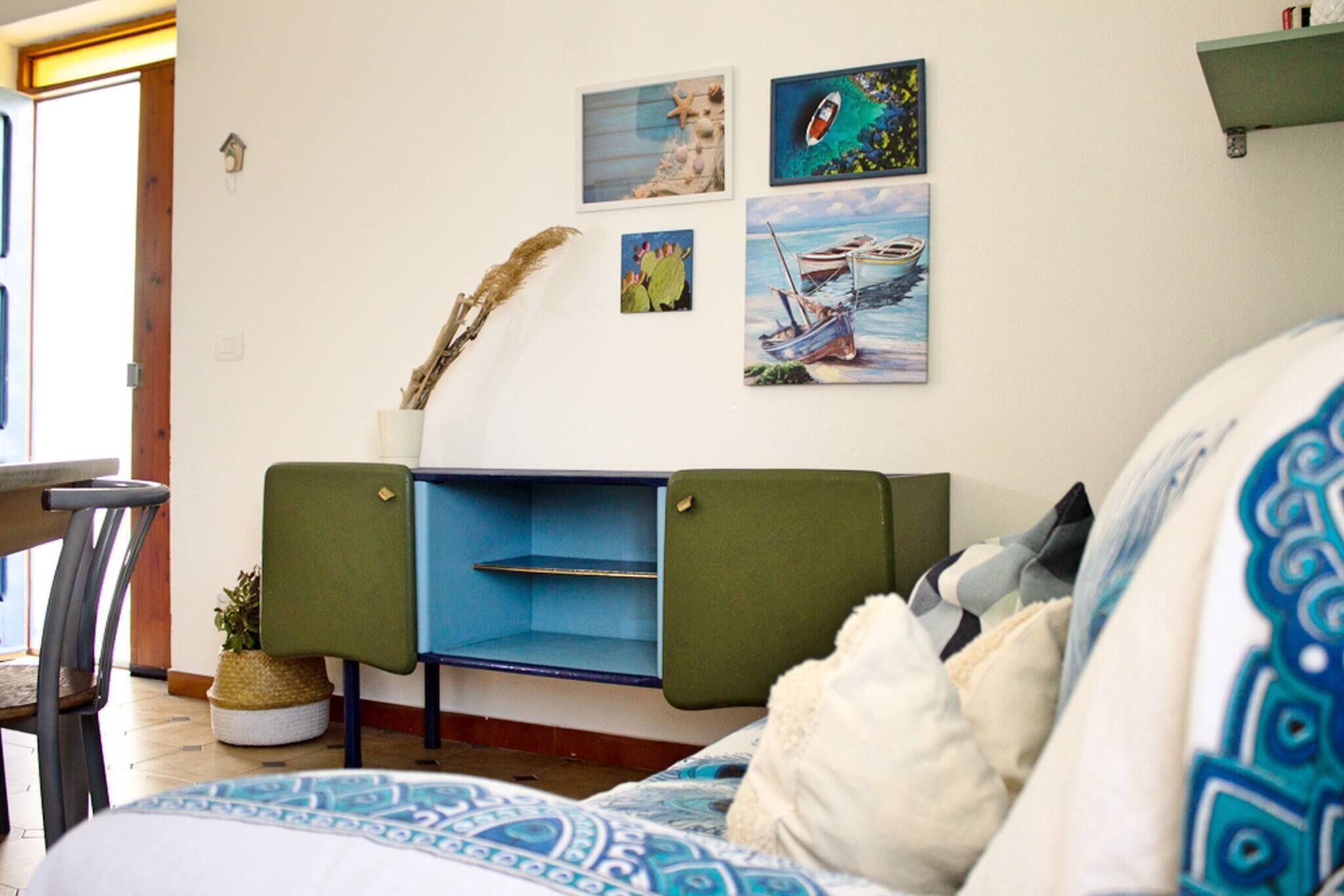 A room with a bed, a green cabinet, a wall with artwork, and a window.